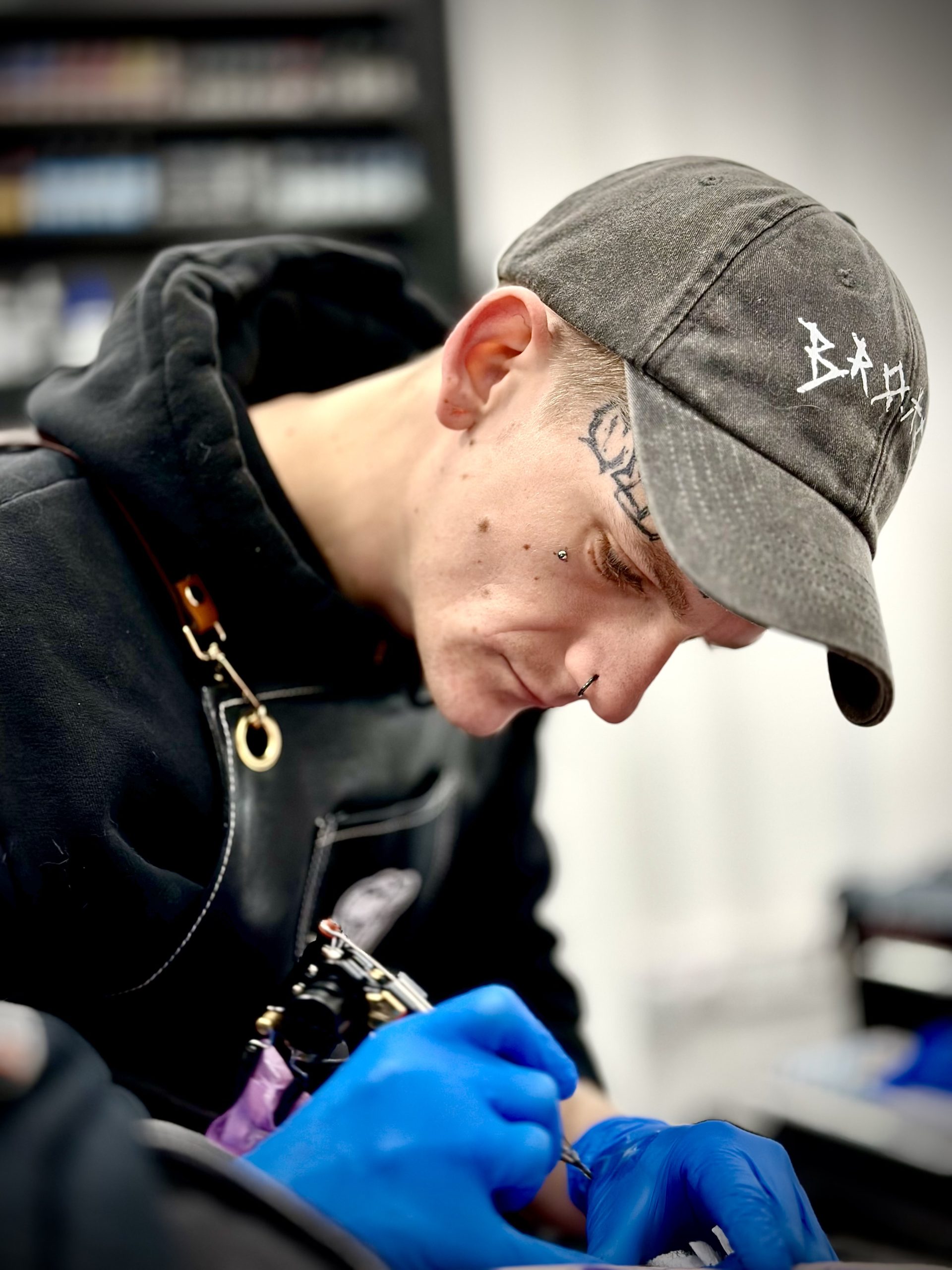 Tattoo artist in a grey cap and black apron focused on tattooing a client